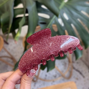 Detail of burgundy glitter acrylic hair claw clip with seven teeth held in hand