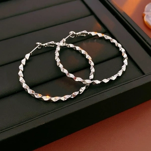 Detailed view of silver hoop earrings with a textured geometric diamond-cut design