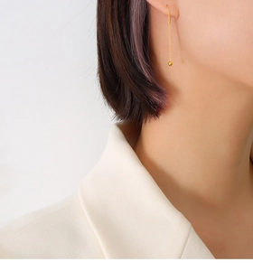 Close-up of minimalist gold drop earrings with delicate chain and polished ball on model