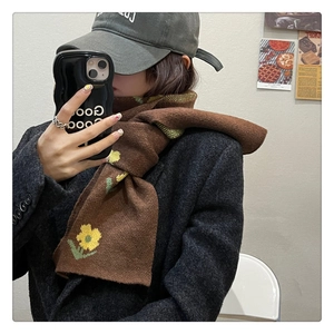 Detail of a brown knitted scarf with yellow floral patterns paired with a wool coat