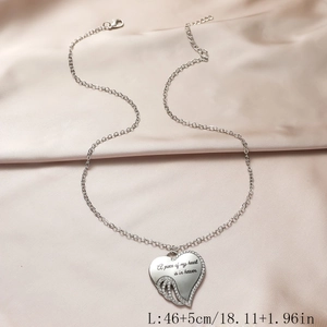 Detail of silver heart necklace with angel wings and memorial text on satin background