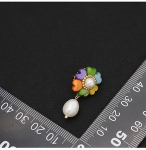 Macro shot of pearl flower earring with heart-shaped petals measured against a scale