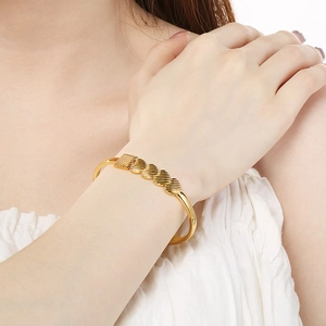 Detailed view of a gold hollow heart-shaped bracelet with striped texture on female wrist