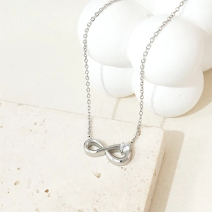 Detailed view of infinity pendant necklace with zircon stone on cream travertine