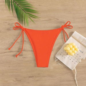 Detail of vibrant orange bikini bottoms with adjustable side ties on a beach decor background