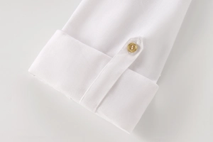 Close-up of white linen shirt sleeve cuff featuring a polished gold button detail
