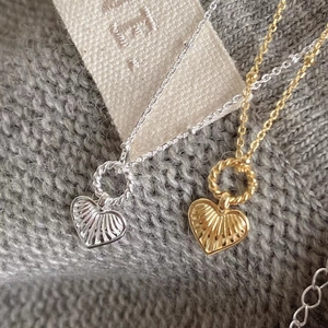 Detailed view of silver and gold heart necklaces with textured radial patterns on fabric