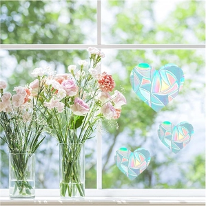 Detailed view of three heart-shaped rainbow prism window stickers reflecting colorful sunlight