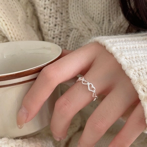 Close-up of minimalist silver heart link ring worn while holding a ceramic cup