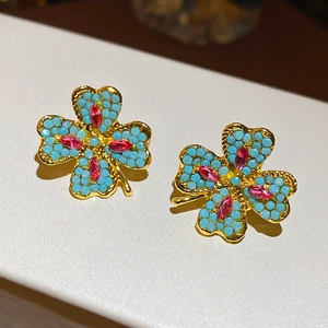 Detailed macro of gold clover earrings with blue turquoise stones and red gemstone center