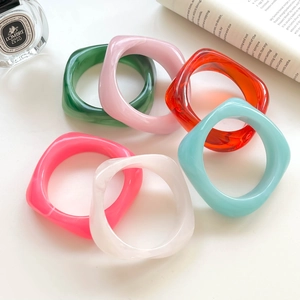 Detailed view of six colorful acrylic resin square bangles styled with lifestyle props