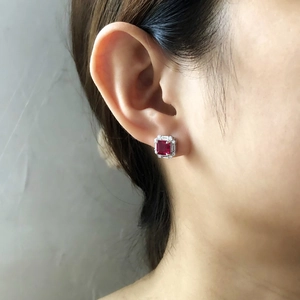 Macro detail of silver stud earrings featuring square red gemstone with halo diamonds