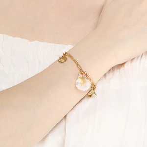 Détail d'un bracelet en or 18 carats avec breloques soleil, coquillage et papillon au poignet