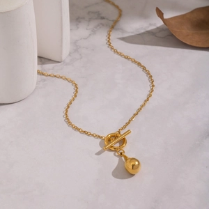 Elegant gold OT buckle necklace with polished metal drop pendant on marble background