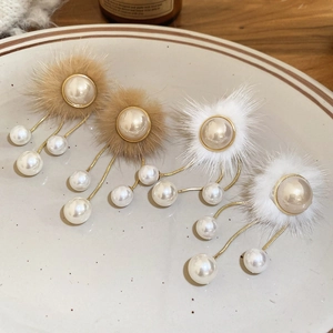 Detail view of plush fur pearl earrings with golden chain tassels on a ceramic plate