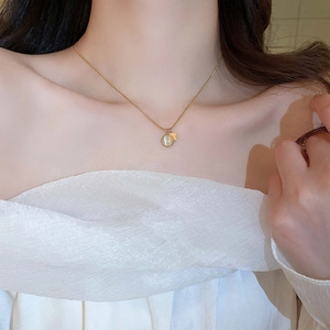 Detailed view of a gold snake chain necklace with opal and round charm on female neck