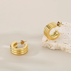 Macro detail of gold ribbed C-shape earrings on stone, showing fine triple-layered texture