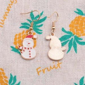 Détail de boucles d'oreilles bonhomme de neige en alliage doré et émail rouge sur tissu