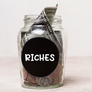 Close-up of a clear glass money jar with Riches label filled with coins and cash