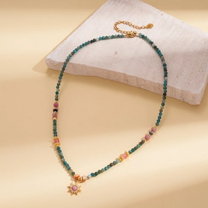 Détail du collier de perles avec pendentif soleil doré sur fond de texture de pierre
