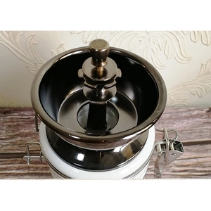 Manual coffee grinder with ceramic body and dark metal bean hopper on wooden surface