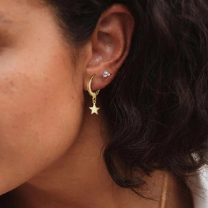 Close-up of model wearing gold hoop earrings with polished star charms on lobe