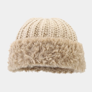 Detail der groben Strickstruktur und des weichen Kunstfellbündchens einer beigen Wintermütze