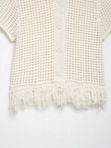 Gros plan détaillé sur la texture crochetée avec boutons et ourlet à franges du cardigan blanc