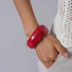 Detail shot of wide dark red acrylic bangle with translucent texture on female wrist