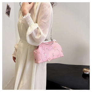 Close-up of pink floral embroidery handbag with metal chain strap on white dress