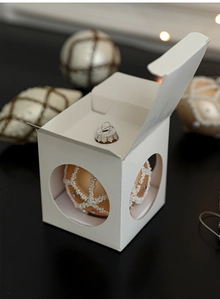 Detailed view of champagne gold Christmas ball with pearls in a white gift window box