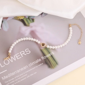 Detail of elegant pearl bracelet featuring a gold heart pendant with zircon inlay