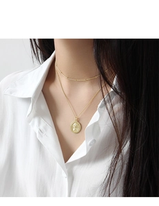 Détail d'un collier doré à deux rangs avec pendentif pièce et chaîne à petites billes