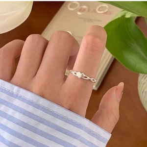 Detailed view of silver heart ring with chain band worn on index finger in natural light