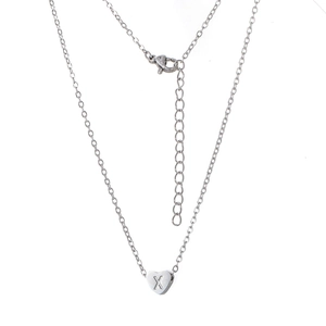 Détail macro du pendentif cœur argenté avec lettre X gravée sur une fine chaîne maille forçat