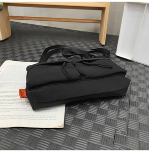 Detail of black nylon messenger bag with dual front pockets and orange side label