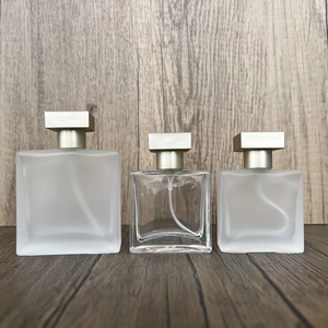 Three clear and frosted glass square perfume spray bottles with gold caps on wood