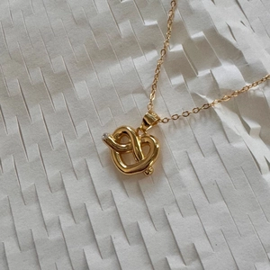 Detailed close-up of golden heart knot pendant necklace with crystal on honeycomb paper