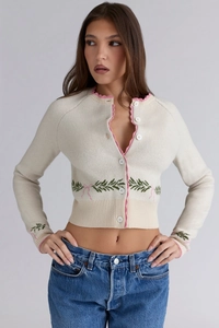 Detail of pink bow jacquard and scalloped lace trim on a white cropped knit cardigan