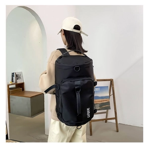Rear view of a model wearing a black large capacity nylon travel backpack with top handle