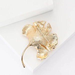 Detailed view of golden ginkgo leaf brooch with natural vein texture on white background