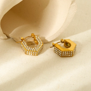 Macro shot of hexagonal gold earrings with white zircon inlays and shiny metal texture