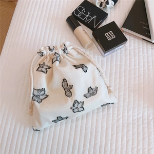 Close-up of cotton linen drawstring pouch with black butterfly embroidery on white bedsheet