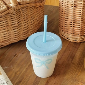 Detail view of a cute reusable plastic cup with a blue bow pattern and matching straw