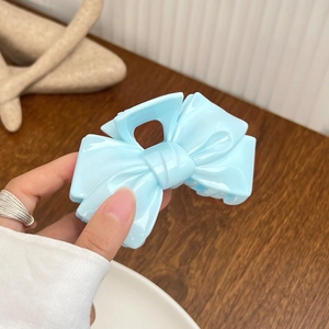 Mint blue ribbon bow hair claw clip in translucent finish held by hand on a wooden desk