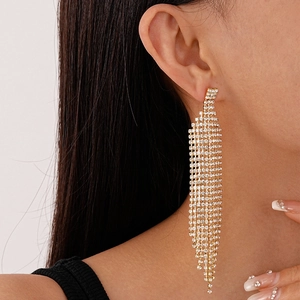 Détail de longues boucles d'oreilles dorées à glands et cristaux sur l'oreille
