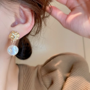 Detail of gold hammer-textured metal earrings with baroque pearl drop on a model
