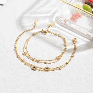 Detail of double-layer gold chain bracelet with heart and round zircon charms