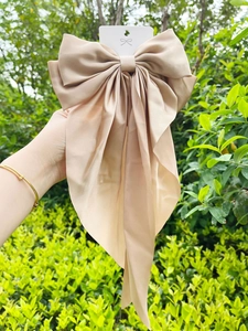 Detail showing oversized champagne gold satin bow hair clip with elegant silk texture