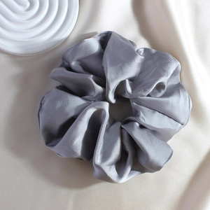 Close-up of a grey satin scrunchie with a soft glossy texture on a rippled plate